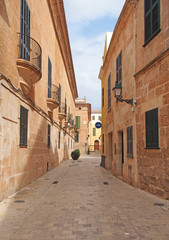 A quiet empty sunlit picturesque cobbled narrow street in ciutadella menorca with balconies and street lamps on colorful old houses