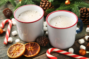 Cappuccino in mugs with oranges and candy cane on wooden table