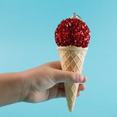 minimal Christmas concept, the baby's hand holds a waffle horn from ice cream, a red Christmas tree...