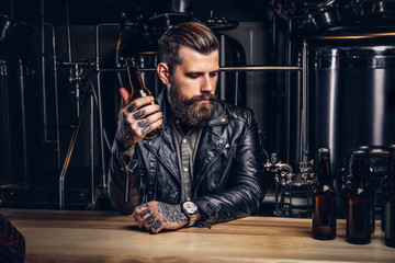 Fototapeta na wymiar Stylish bearded biker dressed black leather jacket sitting at bar counter in indie brewery.