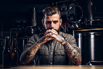 Portrait of a pensive tattooed hipster male with stylish beard and hair in the shirt in indie...