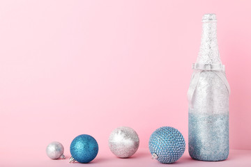 Decorated champagne bottle with christmas baubles on pink background