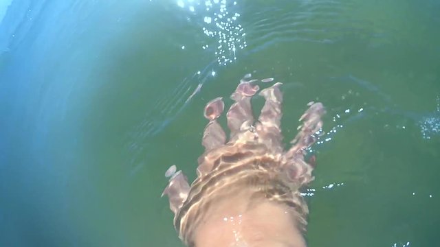 Slow motion POV. Scene point of view the hand glides slides on the surface of the water on a sunny day with natural sunny light rays close-up. Ocean sea summer concept