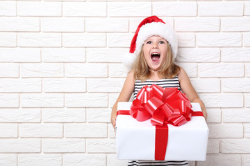 Happy girl holding gift box on brick wall background