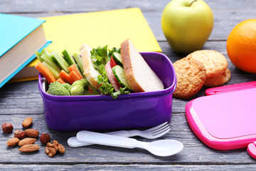 School lunch box with sandwich and vegetables on wooden table