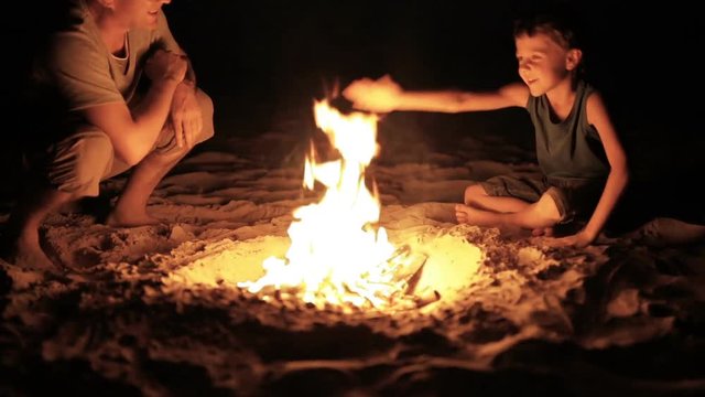 Father and son playing on the beach near the bonfire at the sunset time. Concept of happy friendly family.