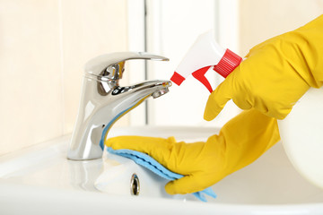 Hands in gloves with sponge and bottle of detergent cleaning water tap in bathroom