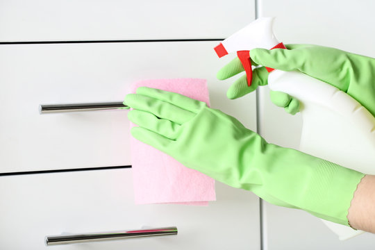 Hands in gloves with rag and bottle of detergent cleaning kitchen drawer