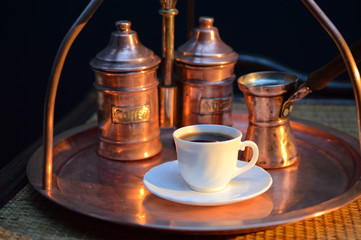 a Cup of coffee near the sugar bowl and a container with coffee on a copper tray and a rattan table