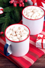 Cappuccino with marshmallows in mugs and fir tree branches on wooden table