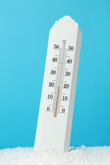 White thermometer in snow on blue background