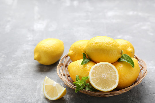 Ripe lemons in basket on grey wooden table