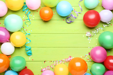 Colorful balloons with confetti on green wooden table