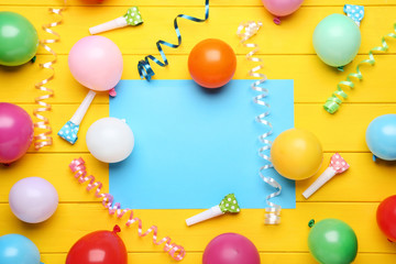 Colorful balloons with sheet of blank paper on yellow wooden table