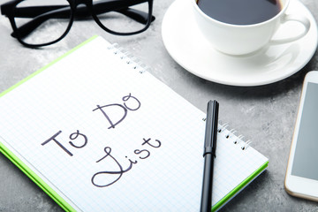 To do list in notepad with cup of coffee and glasses on grey wooden table