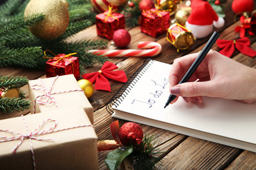 Female hand writing to do list in notepad with christmas decoration on wooden table
