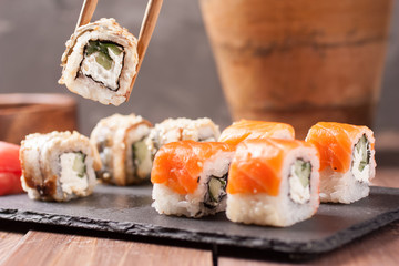 Salmon rolls nigiri in chopsticks over wooden background