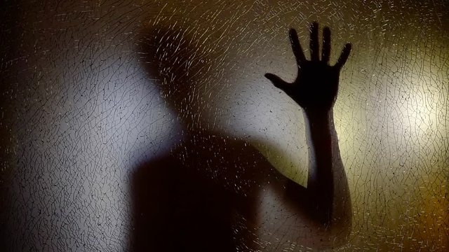 shadow of human figure on a glass screen, holding hand and moving back, silhouette of alien