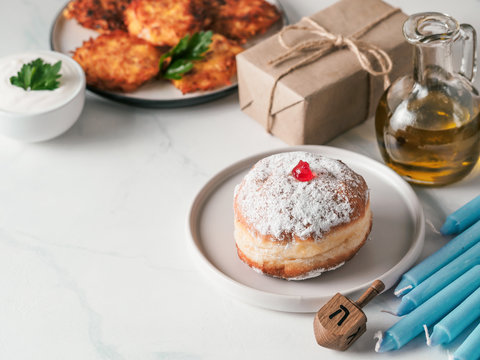 Jewish holiday Hanukkah concept and background. Hanukkah food doughnuts and potatoes pancakes latkes, oil, giftbox, candle and traditional spinnig dreidl on blue background. Copy space for text.