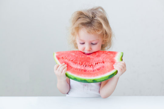 cute little baby girl eating watermelon slice on light background