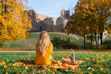 Foto op Plexiglas Woman Sitting Plaid Basket with Food Bakery Autumn Picnic Time Rest Background Old Ruins Background © milenie