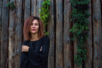 Fototapeta premium Portrait of a beautiful young woman in black dress on a background of old wooden wall