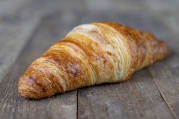 Tasty well-baked croissant on a wooden kitchen table. Light bread prepared for breakfast.
