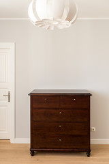 Restored dark brown commode in a modern interior, white wall, copy space.