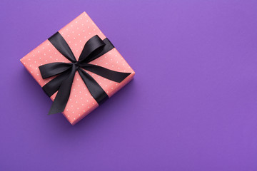 Wrapped gift box with colored ribbon as a present for Christmas, new year, mother's day, anniversary, birthday, party,  on violet background, top view. Present for a colleague at work.
