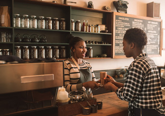 Smiling African barista handing a customer her drink order - obrazy, fototapety, plakaty