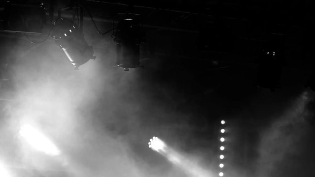 Contrasted black and white scene of bright lights and thick smoke on a black background. Large blank space useful for titling or inclusions. Stage spotlights, dark background and a heavy fog creating 