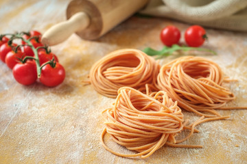 raw homemade colored spaghetti nest with flour on a wooden table. fresh Italian pasta with tomatoes