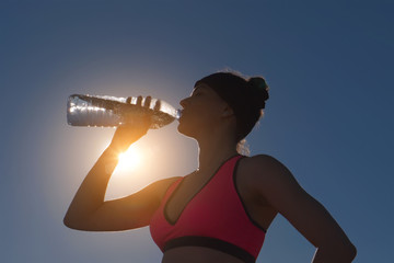 Sport woman drinking water from bottle against the sun