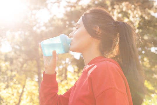 Athletic woman in sporty red clothes drinking water while jogging. Portrait, close-up in the sunset sunlight. silhouette of girl drinking water outdoor