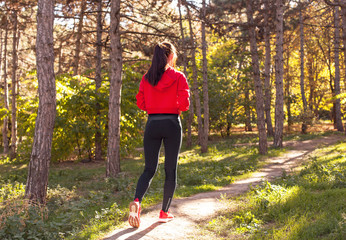 A beautiful, young girl running through the woods during sunset. Athletic woman in sportswear running along a forest trail. Portrait, full length with the forest in the background. View from the back © Mira