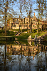 Fototapeta na wymiar Beautiful afternoon light in public park with green grass, building and trees reflecting in pond. Shot in Cesis, Latvia.