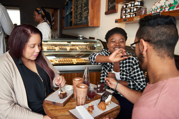 Smiling friends sitting at a cafe table eating desserts together