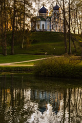 Obraz premium Beautiful afternoon light in public park with green grass, Christ Transfiguration Orthodox Church and trees reflecting in a pond. Shot in Cesis, Latvia.