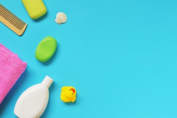 Flat lay bath products. Shampoo, green soap bar, wooden comb, pink towel and yellow rubber duck. Copy space