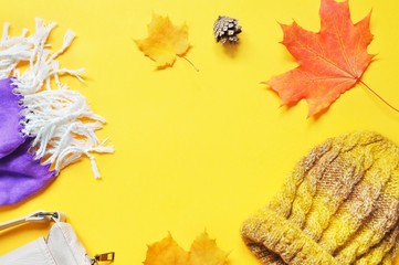 Flat lay autumn mockup. Purple scarf, maple leaves and woolen hat on a yellow background