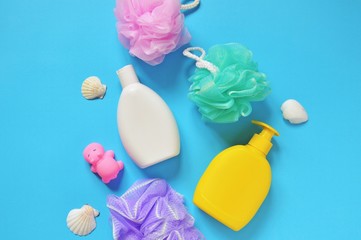 Flat lay baby bath products. Colorful sponges, shampoo bottle, liquid soap, rubber toy hippo and seashells