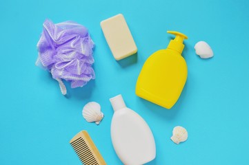 Flat lay photo bath products. Toiletries set. Moisturizing shampoo, yellow liquid soap packaging, purple sponge, wooden comb and seashells on a blue background