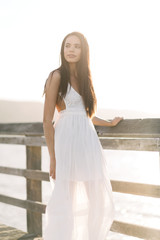 Young woman patiently waiting holding a wooden railing on a pier looking in to the distance during the golden hour sunset.