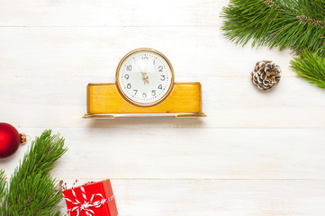 New Year or Christmas background. Retro alarm clock pine branches cones gifts presents toys red ball on white wooden background top view with copy space. Christmas timer Time to celebrate Xmas