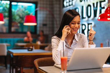 Young business woman talking on the phone in a cafe with a laptop in front of her