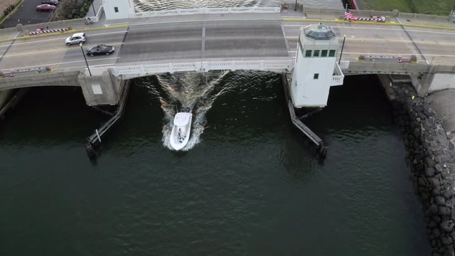 Aerial drone shot at over a bridge and a small white boat heading out into the Atlantic Ocean off the coast of Belmar, New Jersey.