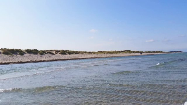 Liseleje Beach by the Tisvilde forest and coastal area on the Danish island of Zealand. People walking in the distant. Springtime with sunny clear blue sky. Pristine clear water with gentle waves.