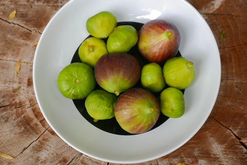 A black and white bowl with green and purple figs on a tree stump, flat lay