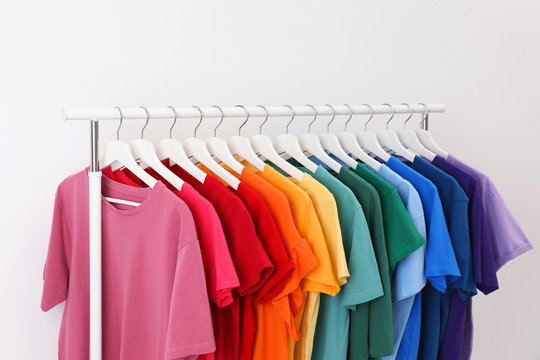 Rack with bright clothes on white background. Rainbow colors