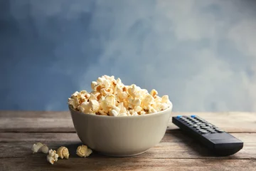 Tuinposter Bowl of popcorn and TV remote on table against color background. Watching cinema © New Africa